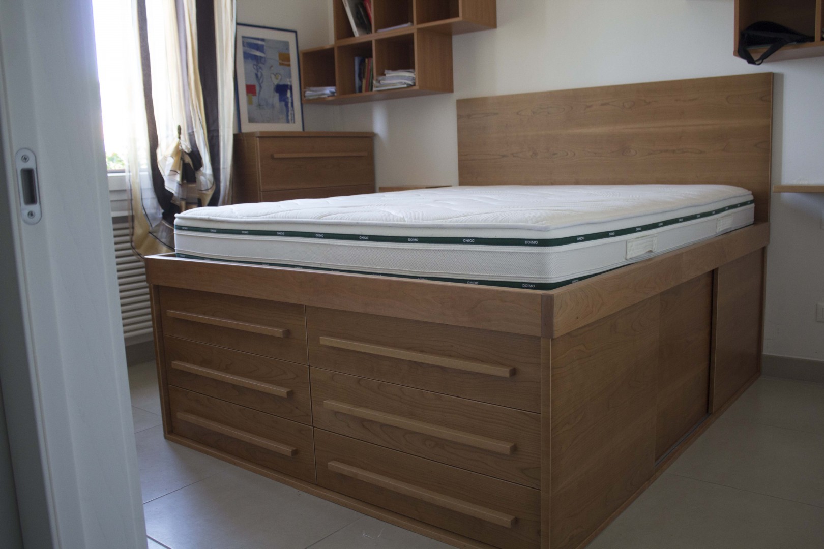 Arredamento su misura realizzato da Profili - Falegnameria & Design. Letto contenitore moderno in legno salvaspazio su misura con cassettoni e ante scorrevoli.