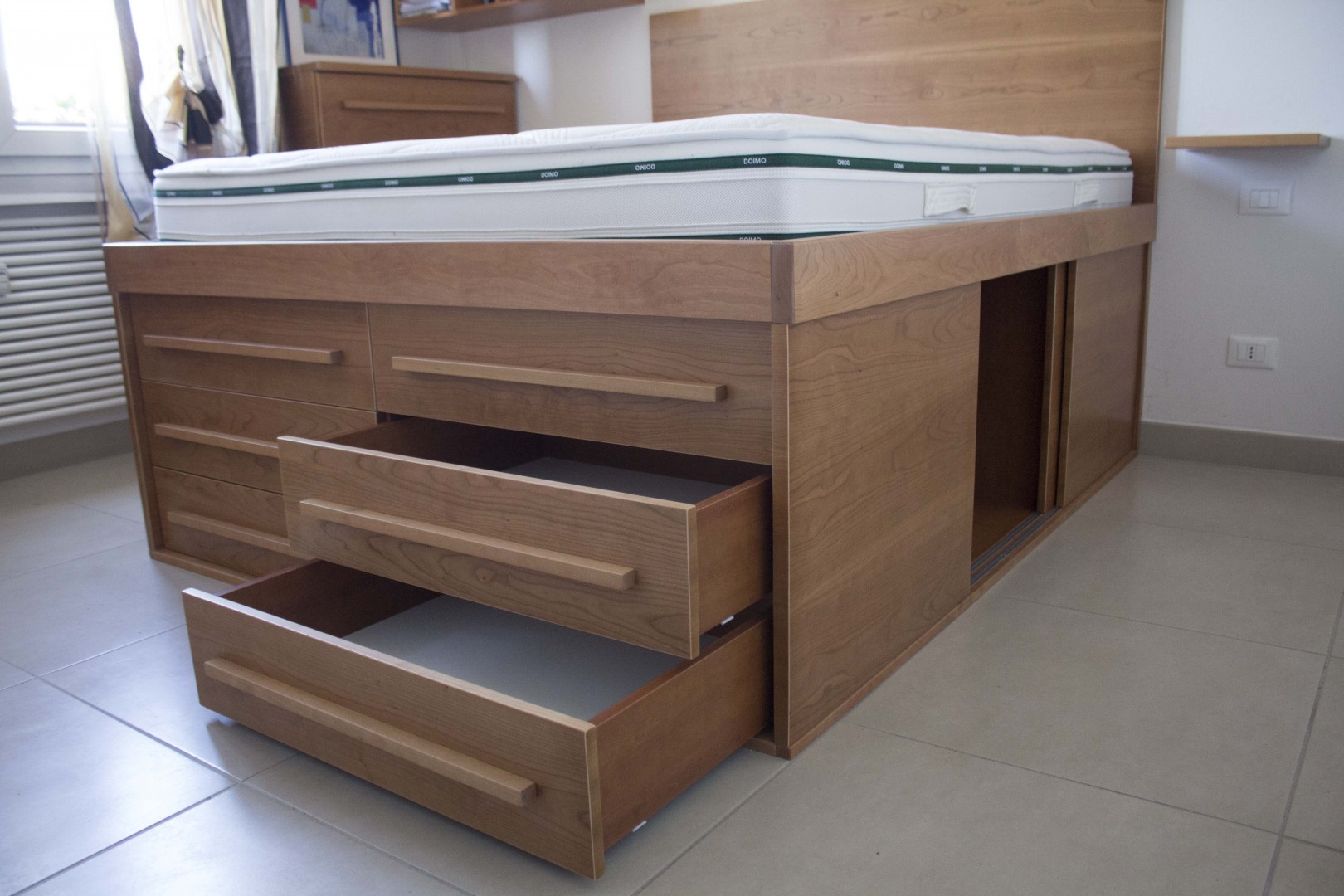 Arredamento su misura realizzato da Profili - Falegnameria & Design. Letto contenitore moderno in legno salvaspazio su misura con cassettoni e ante scorrevoli.