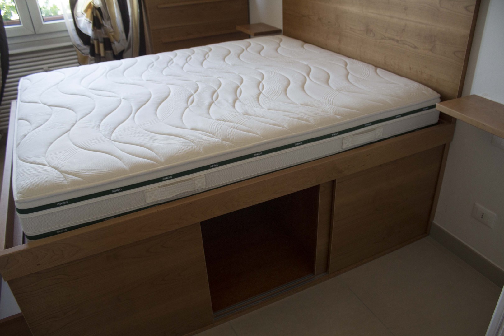 Arredamento su misura realizzato da Profili - Falegnameria & Design. Letto contenitore moderno in legno salvaspazio su misura con cassettoni e ante scorrevoli.